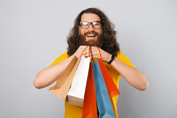 Photo of happy hipster man with long hair and beard holding many colorful paper shopping bags.