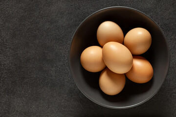 Eggs chicken whole beige in bowl, on dark background, top view, space to copy text.