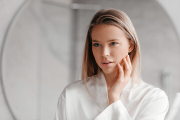 Natural beauty. Attractive lady looking at her reflection in mirror and touching perfect skin,...