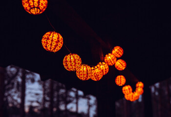 Cute orange color ball shape paper lantern string lights illuminated and hanging on home balcony at night.