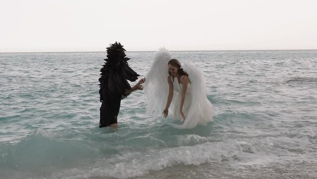 Black and white angels. female models in images of black and white angels with wings holding hands have fun in sea water.