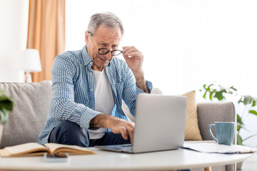 Mature man squinting using laptop, looking at pc screen