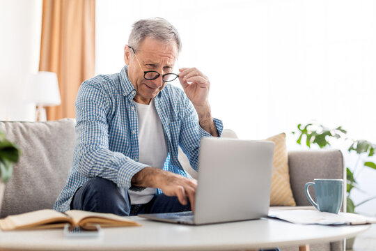 Mature man squinting using laptop, looking at pc screen