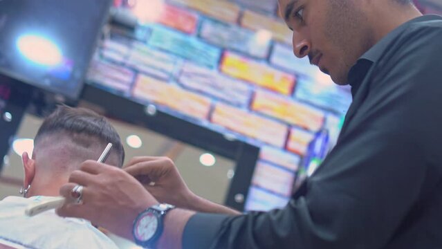 Young Arab barber cuts man's hair with a straight-edge razor in a barbershop. Men's hairstyling and haircutting in the salon. 