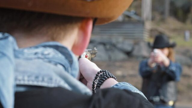 Cowboy and cowgirl in duel, pointing guns at each other.