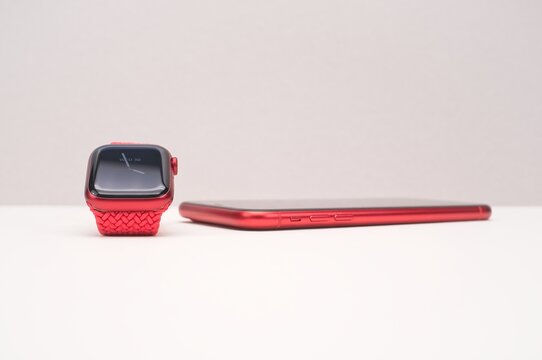 Apple Watch And Iphone Product Red On A White Table Against A Gray Wall With Space For Text