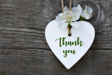 Thank You or thanks greeting card with cherry flowers and decorative white heart on old wooden background.International Thank You Day concept.