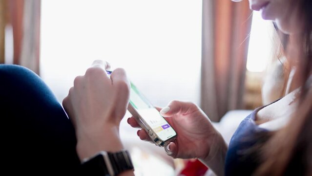 Online shopping concept. Young woman sitting on the bed and makes online shopping on a smartphone. Woman at Home Lying on Couch in Living Room Using Smartphone Buys in Internet Shop.