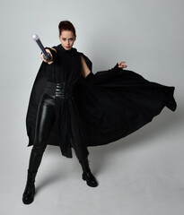 Full length portrait of pretty redhead female model wearing black futuristic scifi leather cloak...