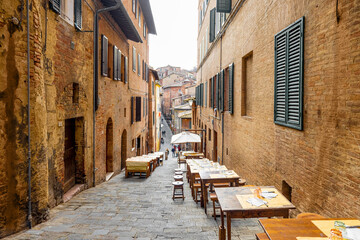 Fototapeta na wymiar View on narrow and cozy street in the old town of Siena city in Italy. Concept of ancient architecture of the Tuscan region