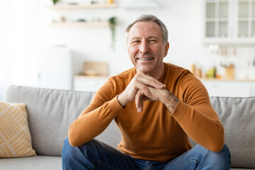 Smiling mature man sitting on the couch and posing