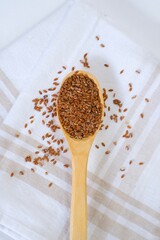 Isolated flax seeds in a wooden spoon on a linen napkin on a white table. Ingredient for flaxseed porridge and jelly. Minimalistic simple natural light template. Superfood. Organic eco healthcare.