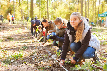 Group of volunteers and children planting a tree in the forest