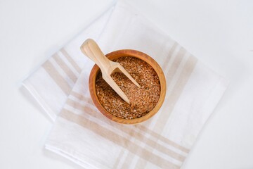 Flax seeds in a round plate with wooden spoon on a linen napkin in a kitchen. Ingredient for flaxseed porridge and jelly. Minimalistic simple natural light template. Superfood. Organic eco healthcare.
