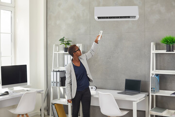 Woman turns on the AC at work. Black businesswoman standing in a modern office interior, holding a...