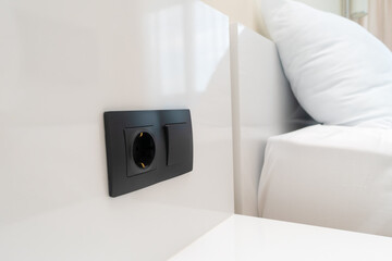 Close-up of a black switch and socket on a white wall near the bed