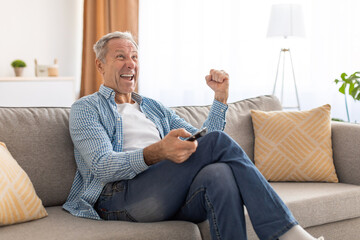 Excited senior man watching tv celebrating goal holding remote control - Powered by Adobe