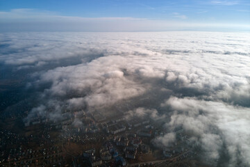 Aerial view from high altitude of distant city covered with puffy cumulus clouds flying by before rainstorm. Airplane point of view of landscape in cloudy weather