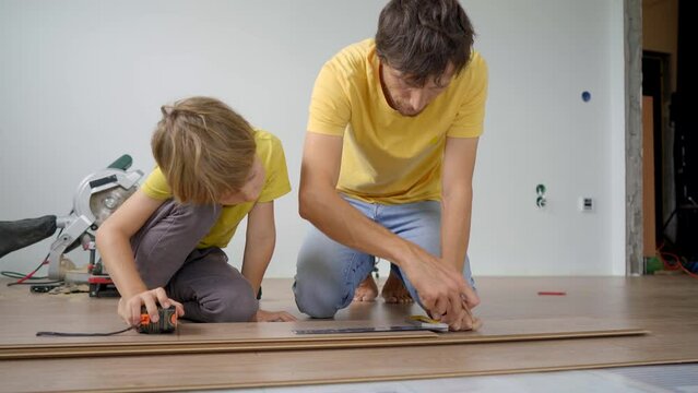 Father and his little son install laminate on the floor in their apartment. DIY concept
