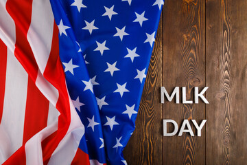 the word MLK day laid with silver metal letters on wooden surface with crumpled USA flag at left...