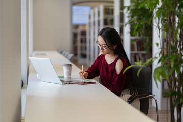 Smart student girl sit at desk make notes from laptop search or read information, prepare for examination. Female do homework create essay or practice subject. Studying process and education concept