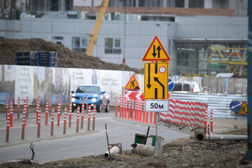 Roadworks warning traffic signs of construction work on city street and slowly moving cars