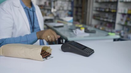 Close shot of customer buying medicine by paying money by tapping smartwatch on swiping machine at pharma store - concept of wireless transaction, digital payment and modern technology. - Powered by Adobe