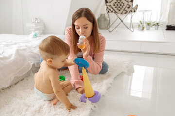 Young mom enjoying time with her kid while playing in bedroom
