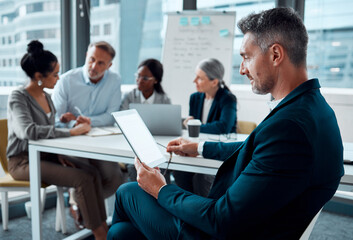Fototapeta premium .. Shot of a mature businessman using a digital tablet in an office with his colleagues in the background.