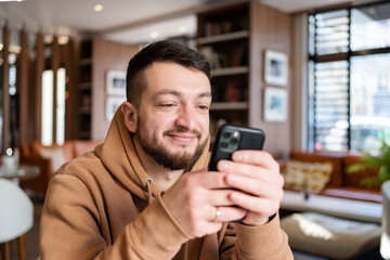 Young man sitting and using smartphone at coffee shop.Cheerful hipster guy at the cafe using a mobile phone.