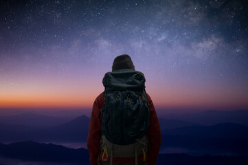 Silhouette of young traveler wearing sweater with backpack standing alone on top of the mountain...