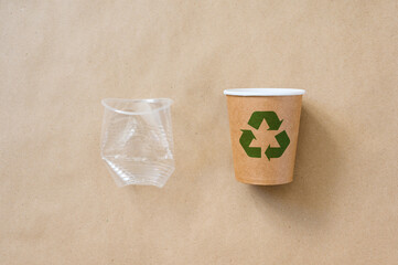 A crumpled plastic cup next to an eco-friendly paper cup with a green recycling symbol. The concept...