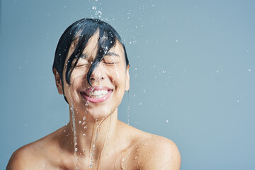 Wake up to the refreshing sensation of water. Shot of a young woman having a refreshing shower against a blue background. - obrazy, fototapety, plakaty