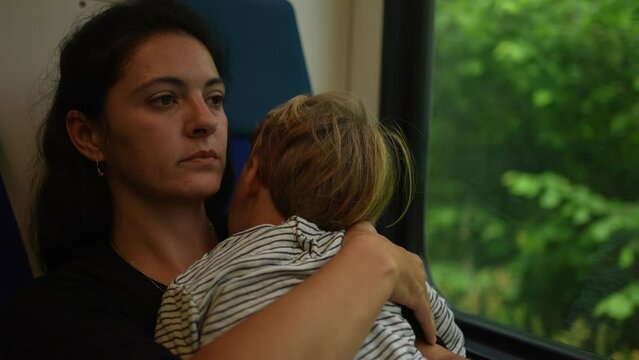 Parent falling asleep traveling by train with sleeping toddler in arms