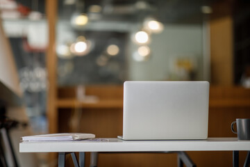 Laptop Computer, notebook, and eyeglasses sitting on a desk in a large open plan office space after working hours	