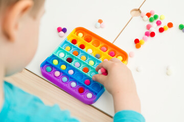 Child plays with sensory fidget toy Pop-it. Instrument for fine motoric skils, tool to start...