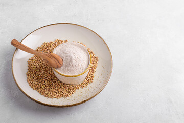 Buckwheat flour in a ceramic bowl with spoon and raw green buckwheat grain on a ceramic plate on light grey concrete background, top view. Alternative flour, gluten free flour, healthy nutrition