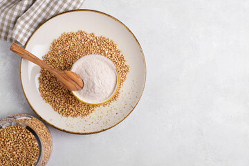 Buckwheat flour in a ceramic bowl with spoon and raw green buckwheat grain on a ceramic plate on light grey concrete background, top view. Alternative flour, gluten free flour, healthy nutrition