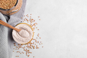 Buckwheat flour in a ceramic bowl with spoon and raw green buckwheat grain in a jar on light grey concrete background, close up, copy space. Alternative flour, gluten free flour, healthy nutrition