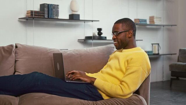 Young male working on a laptop on the couch. Male typing with laptop on couch
