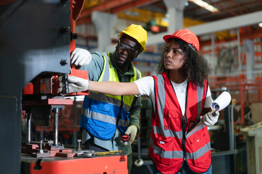 Female and Male engineers in safety vest checking and repairing machine at factory.Preventive Maintenance concept