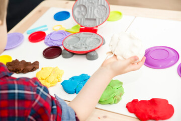 Obraz na płótnie Canvas Cooking with play dough. Kid plays with different color plasticine and plastic kitchen equipment. Artistic face expression of little boy.