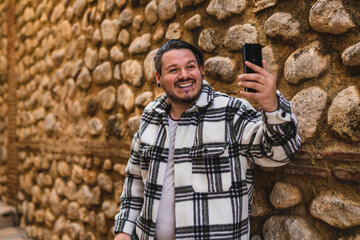 Chico con camisa cuadros blanca posando y tomándose fotos en callejón de piedra en pueblo blanco...