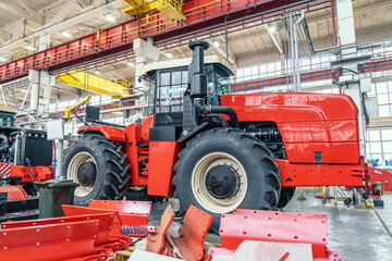 Big red harvester or tractor in process of being assembled on production line at factory for production manufacturing of agricultural machinery.
