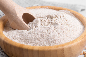 Buckwheat flour in a wooden bowl with wooden scoop and raw green buckwheat grain on light grey...