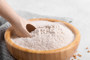 Buckwheat flour in a wooden bowl with wooden spoon and raw green buckwheat grain and napkin on...