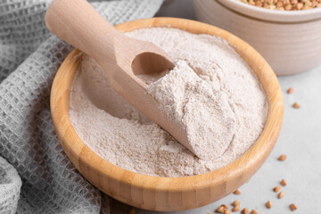 Buckwheat flour in a wooden bowl with wooden scoop and raw green buckwheat grain on light grey table stone background, close up. Alternative flour, gluten free flour, healthy nutrition