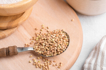 Raw green buckwheat grain in a spoon with wooden bowl on wooden cutboard, close up, top view, copy space. Alternative gluten free food, healthy nutrition