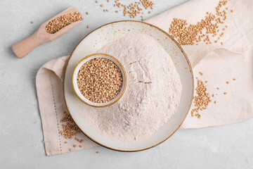 Buckwheat flour in a ceramic plate and raw green buckwheat grain on a bowl and wooden scoop on light grey concrete background, top view. Alternative flour, gluten free flour, healthy nutrition