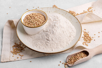 Buckwheat flour in a beige ceramic plate and raw green buckwheat grain on a bowl and wooden scoop...